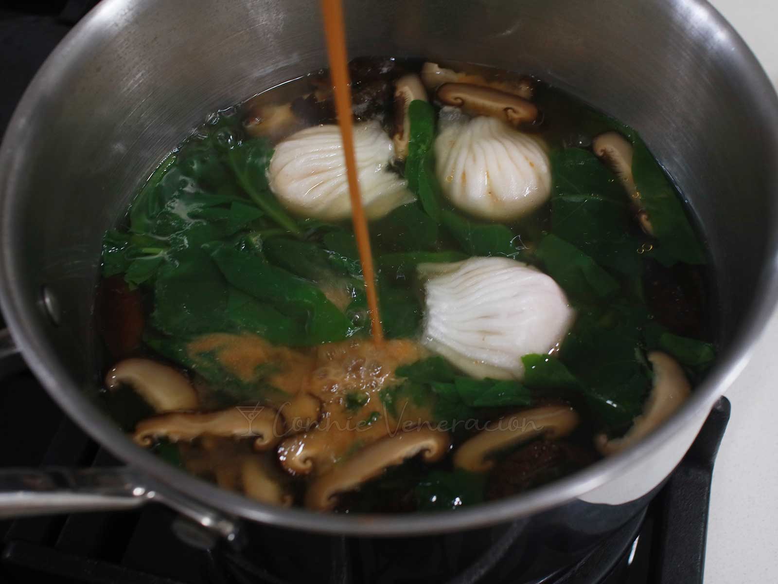 Adding miso to dumplings, mushrooms and spinach in pot