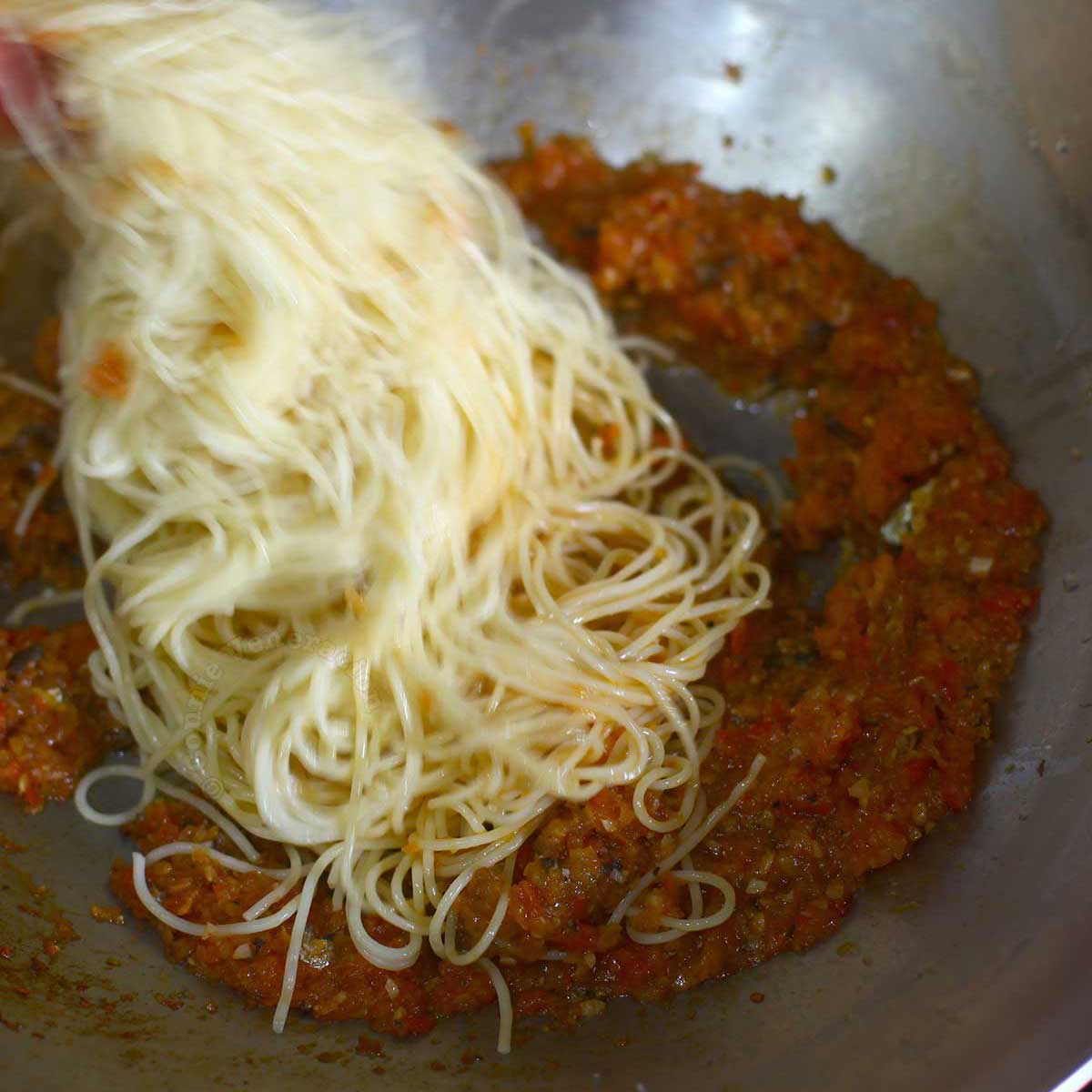 Adding cooked pasta to brandied sardine tomato sauce