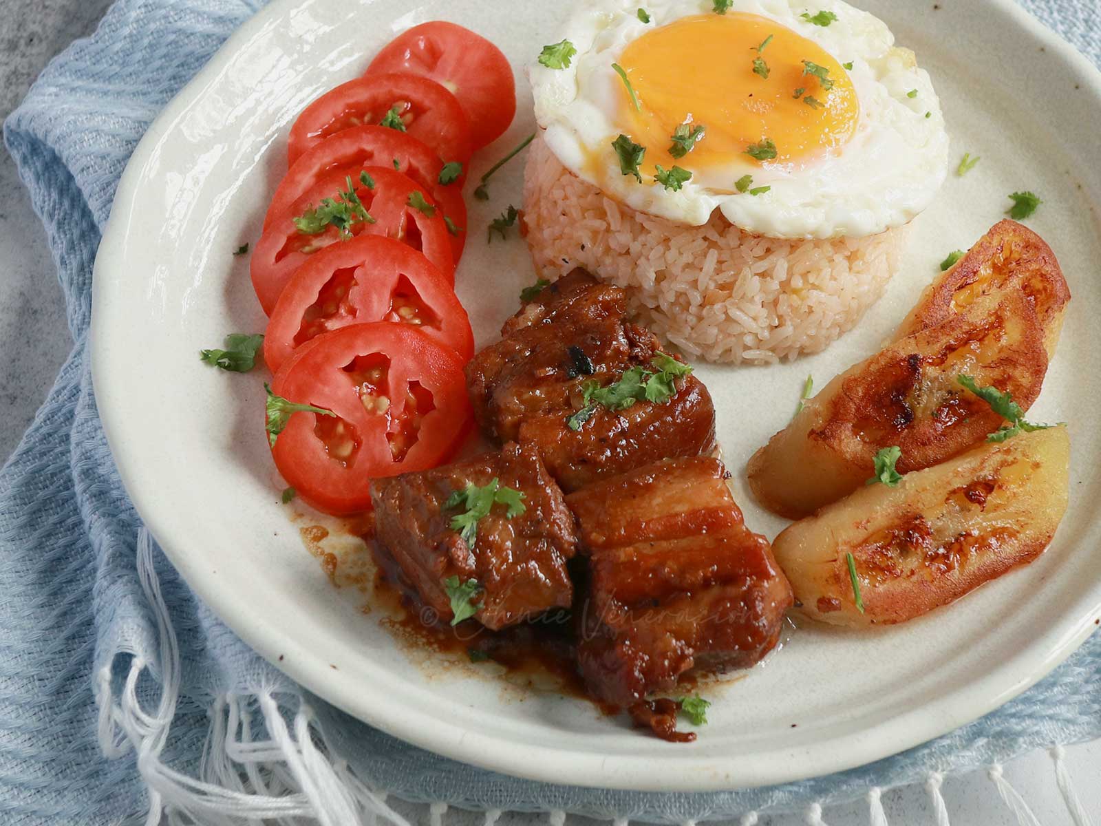 Slow cooker Filipino pork adobo with rice, egg, tomato slices and fried saba bananas