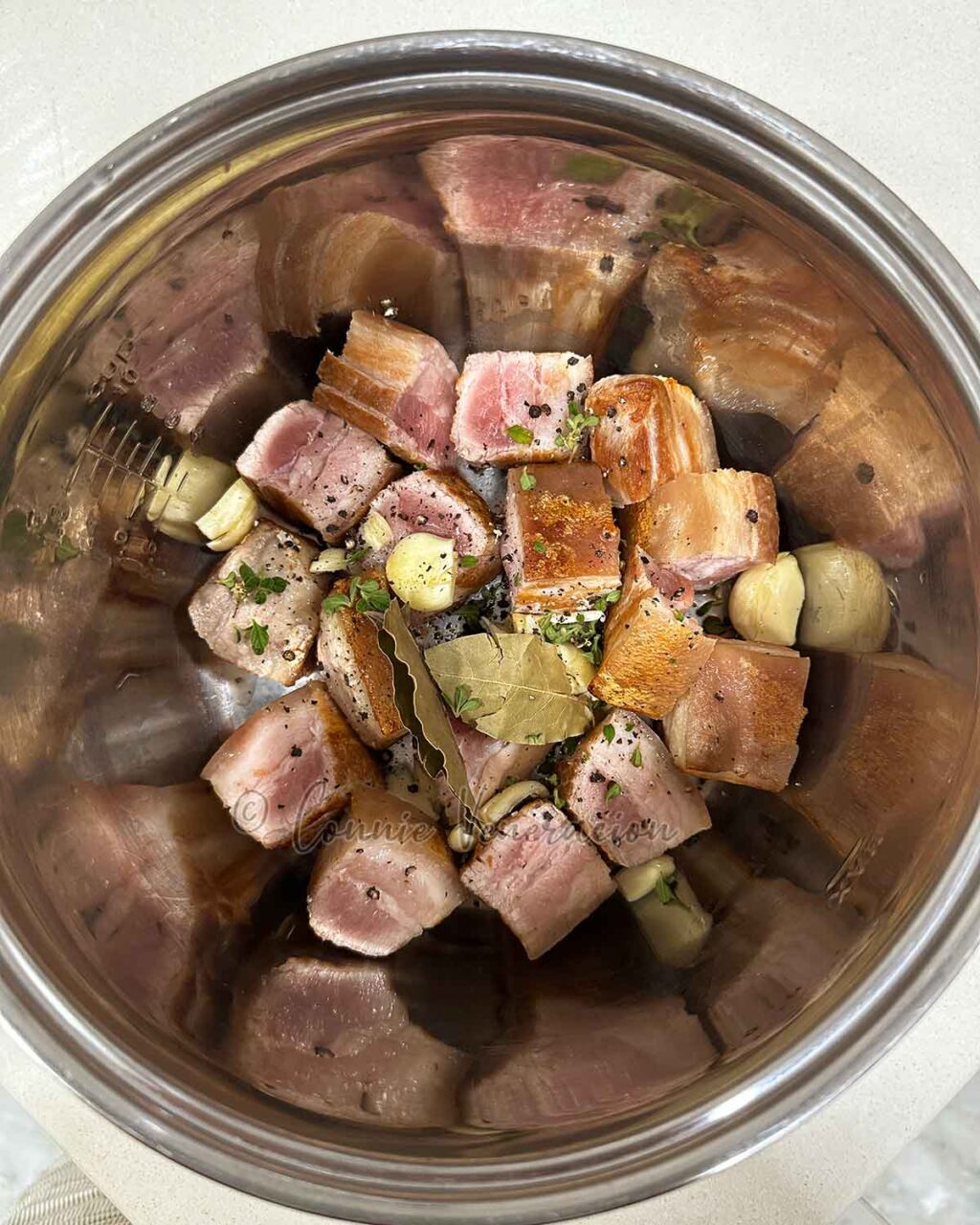 Cubes of browned pork belly with oregano, garlic, pepper and bay leaves in the slow cooker