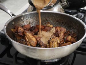 Pouring diluted peanut butter into pot of pork and chicken adobo
