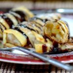 Baked apple spring rolls garnished with chocolate and powdered sugar