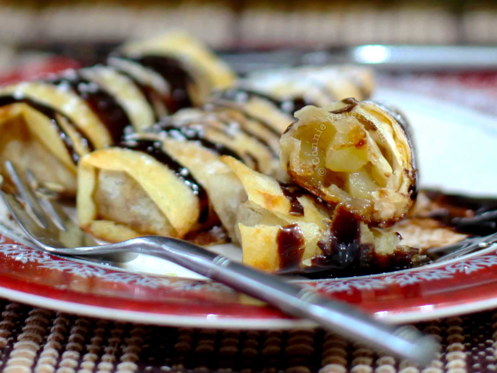Baked apple spring rolls garnished with chocolate and powdered sugar