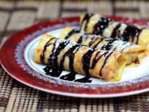 Baked apple spring rolls garnished with chocolate and powdered sugar