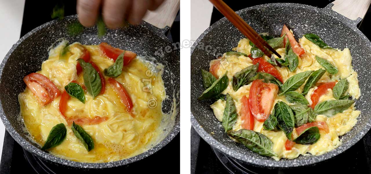 Stirring in basil to scrambled eggs and tomato in pan.