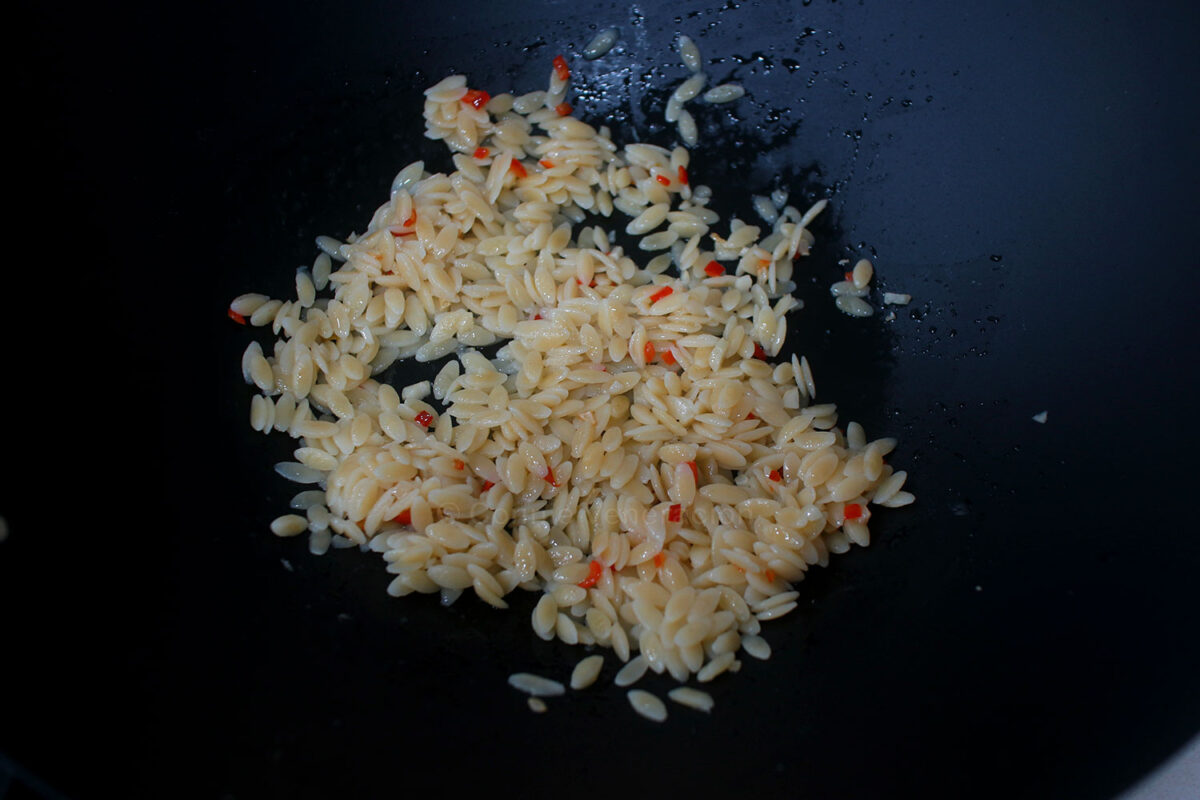 Tossing cooked orzo in spicy olive oil