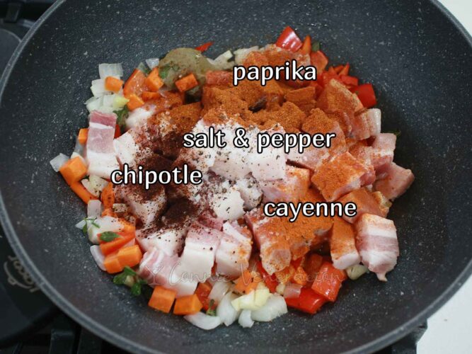 Paprika, salt, pepper, chipotle and cayenne sprinkled over pork in pan