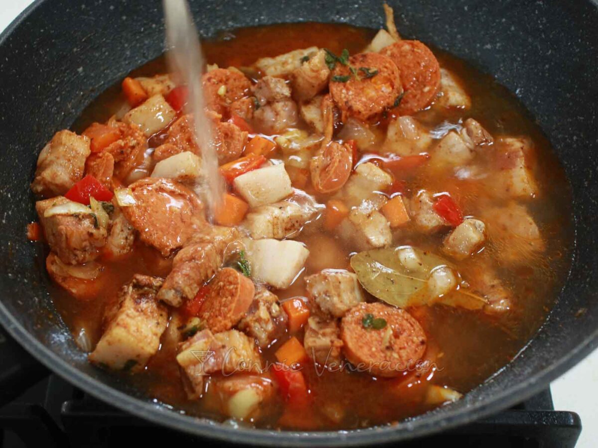 Pouring broth into pan with pork and sausages