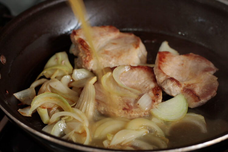 Pouring orange juice into pan with browned pork chops and onion