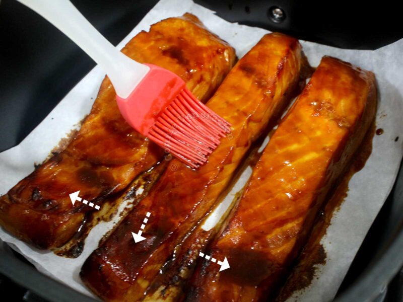 Brushing half-cooked salmon fillets with reduced teriyaki sauce